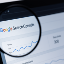 Imagine care ilustrează actualizările Search Console, cu interfața de analiză observată printr-o lupă pe ecranul unui laptop