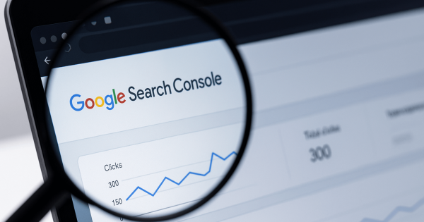 Imagine care ilustrează actualizările Search Console, cu interfața de analiză observată printr-o lupă pe ecranul unui laptop